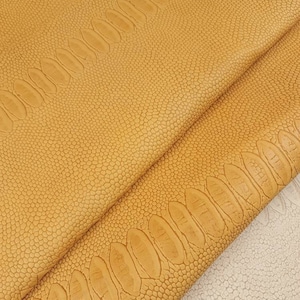 May include: Close-up of a textured, yellow faux leather fabric with a subtle embossed pattern. The fabric is folded in half, revealing the underside.