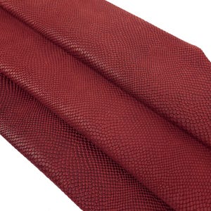 May include: A close-up of a piece of red snakeskin leather. The leather has a textured surface and is folded in thirds.