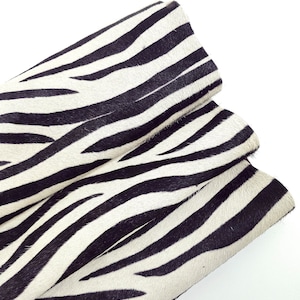 Puede incluir: Primer plano de una tela doblada con estampado de cebra. La tela presenta un patrón de rayas negras sobre un fondo blanco. La textura parece suave, posiblemente de piel animal.
