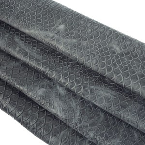 Puede incluir: Tela de imitación de cuero gris con un patrón texturizado de escamas. La tela está doblada en tres partes, mostrando el patrón desde diferentes ángulos.
