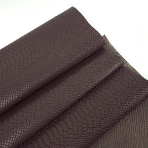 Könnte beinhalten: Nahaufnahme eines dunkelbraunen Kunstleders mit Schlangenhautmuster. Der Stoff ist in mehreren Schichten gefaltet, wodurch die Textur und die Details des Materials sichtbar werden.