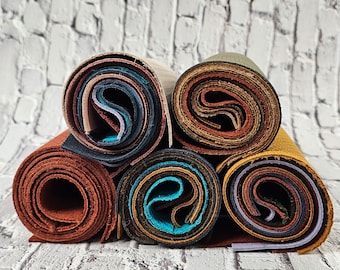 May include: A stack of six rolled up pieces of fabric in various colours, including brown, blue, green, and beige. The fabric is arranged in a circle on a white brick background.