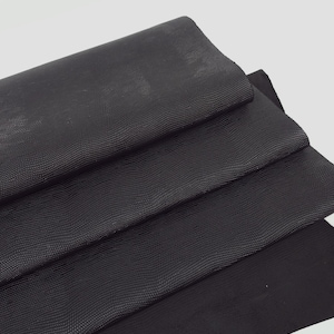 May include: Three pieces of black leather with a textured, embossed pattern. The leather is folded in a stack.