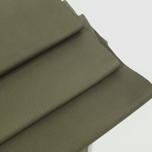 May include: Close-up of olive green leather sheets with a textured, reptile-like pattern. The sheets are layered, revealing the edges and the underside of the leather. The color is a muted, earthy tone.