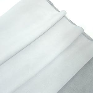 Pode incluir: Close-up de várias folhas de couro branco dobradas. O couro tem uma aparência macia e texturizada, com variações sutis de tom. As bordas das folhas são visíveis, revelando um verso cinza. A impressão geral é de material de alta qualidade.
