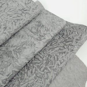 May include: Close-up of several sheets of gray leather with a textured, wrinkled surface. The leather has a soft, suede-like texture on the underside. The material appears to be folded over itself, revealing the different layers of the fabric.
