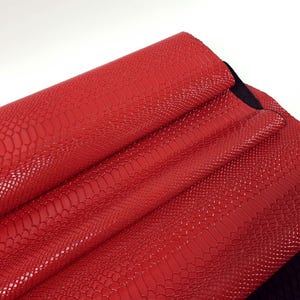 Può includere: Pelle sintetica rossa con un motivo a pelle di serpente. La pelle è piegata in tre e i bordi sono visibili.