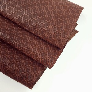 May include: Close-up of a brown fabric with a geometric pattern. The fabric is folded in thirds and has a textured surface.