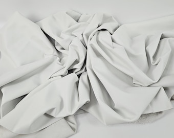 May include: A large piece of white fabric, heavily draped and folded, creating a textured appearance. The material appears soft and pliable, with visible folds and shadows. The fabric is likely used for clothing or home decor.