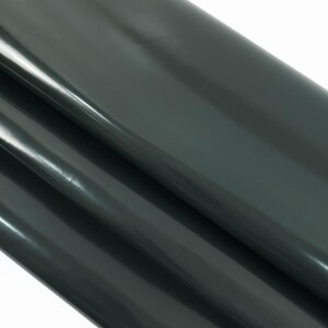 May include: A roll of dark gray vinyl fabric with a glossy finish. The material is folded over itself, creating multiple layers and highlighting the sheen of the surface. The fabric appears smooth and reflective, suitable for various crafting projects.
