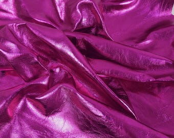 May include: A close-up of a sheet of shiny, magenta-colored fabric. The material is crumpled and folded, creating shadows and highlights that emphasize its texture. The fabric has a metallic sheen.
