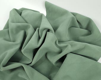 May include: A soft, sage green fabric draped and folded on a white surface.