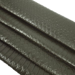 May include: Close-up of a dark green snakeskin fabric with a textured pattern. The fabric is folded in layers, showing the texture and colour.