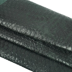 Könnte beinhalten: Nahaufnahme eines dunkelgrünen Lederstoffs mit einer strukturierten, schuppigen Textur. Der Stoff ist an mehreren Stellen gefaltet, wodurch die Textur des Materials sichtbar wird.