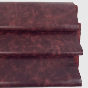 May include: A stack of three folded layers of deep burgundy leather. The material features a smooth, matte surface with subtle, natural variations in color and texture, showing a rich, dark red tone throughout the layered hide material.