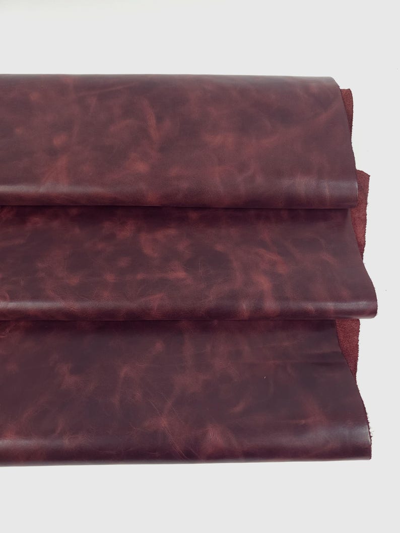 May include: A stack of three folded layers of deep burgundy leather. The material features a smooth, matte surface with subtle, natural variations in color and texture, showing a rich, dark red tone throughout the layered hide material.