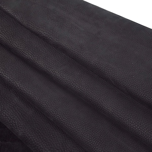 May include: Close-up of black textured leather. The leather has a pebbled surface and is folded in a few places.