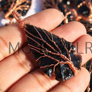 May include: Black obsidian stone pendant with a copper wire tree design. The pendant is shaped like a leaf and has a shiny, black finish.