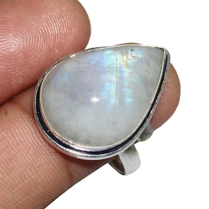 May include: A silver ring with a teardrop-shaped moonstone. The stone is white with a rainbow sheen.