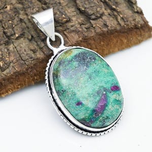 May include: Oval pendant with a green and purple stone set in a silver-colored metal frame. The stone has a mottled appearance with a mix of green and purple hues. The pendant has a loop for a chain.