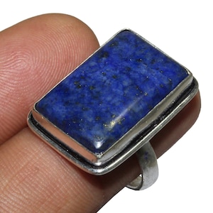 Op de afbeelding: Een zilveren ring met een rechthoekige blauwe lapis lazuli edelsteen. De edelsteen heeft een gevlekt patroon en is gezet in een zilveren zetting.