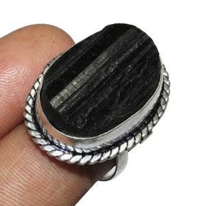 以下が含まれることがあります： 黒い楕円形の宝石が付いた銀の指輪。指輪はバンドの周りに編まれたデザインが施されています。