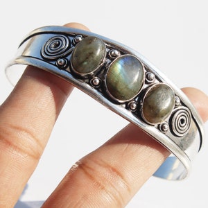 Pode incluir: Pulseira de punho de prata com três pedras ovais de labradorite. A pulseira apresenta um design de espiral e pequenas contas de prata. As pedras de labradorite exibem tons de cinza, verde e azul. Circunferência de aproximadamente 17 cm.