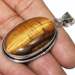 May include: A silver pendant with a large oval-shaped tiger's eye gemstone. The gemstone has a golden brown color with a chatoyant effect.