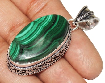 May include: A green malachite gemstone pendant with a silver setting. The pendant has an oval shape and is surrounded by a decorative silver border.