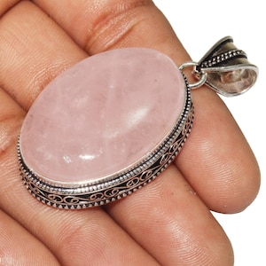 May include: A silver pendant featuring an oval-shaped rose quartz gemstone. The pendant has an intricate silver design around the edge of the stone.