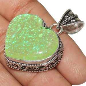 Op de afbeelding: Een zilveren hartvormige hanger met een groene opaal edelsteen. De hanger heeft een ingewikkeld zilveren ontwerp rond de rand.