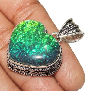 Könnte beinhalten: Ein silberner herzförmiger Anhänger mit einem grün-blauen, irisierenden Opal-Edelstein. Der Anhänger hat eine verzierte silberne Öse.