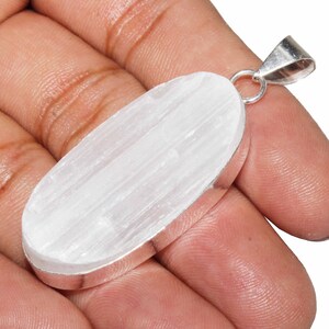 May include: A white selenite crystal pendant with a silver oval setting and a silver bail. The pendant is approximately 2 inches long.