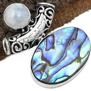 以下が含まれることがあります： 青と緑のアワビの貝殻と白いムーンストーンが付いたシルバーのペンダント。ペンダントは装飾的で華やかなデザインです。