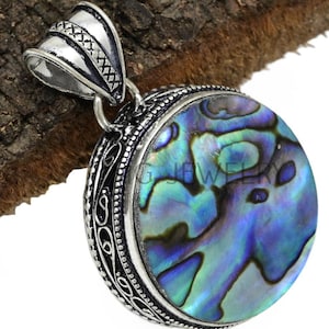 May include: A circular pendant with a silver-coloured metal frame and bail. The pendant has an iridescent abalone shell centre with blue, green, and purple hues. The frame has an ornate, detailed design.