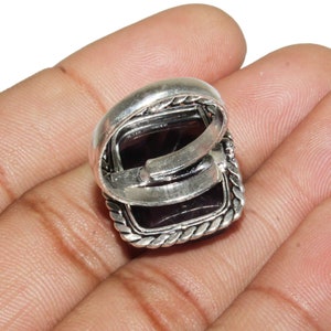 May include: A silver ring with a square-shaped purple gemstone set in a silver bezel. The ring has a decorative rope-like border around the gemstone.