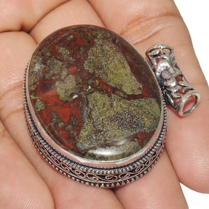 Op de afbeelding: Een zilveren hanger met een groene en rode jaspis steen gezet in een sierlijk zilveren frame. De hanger heeft een lus om een ketting aan te bevestigen.