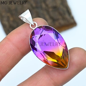 May include: A teardrop-shaped pendant with a purple, pink, and orange gemstone set in sterling silver. The pendant is on a finger.