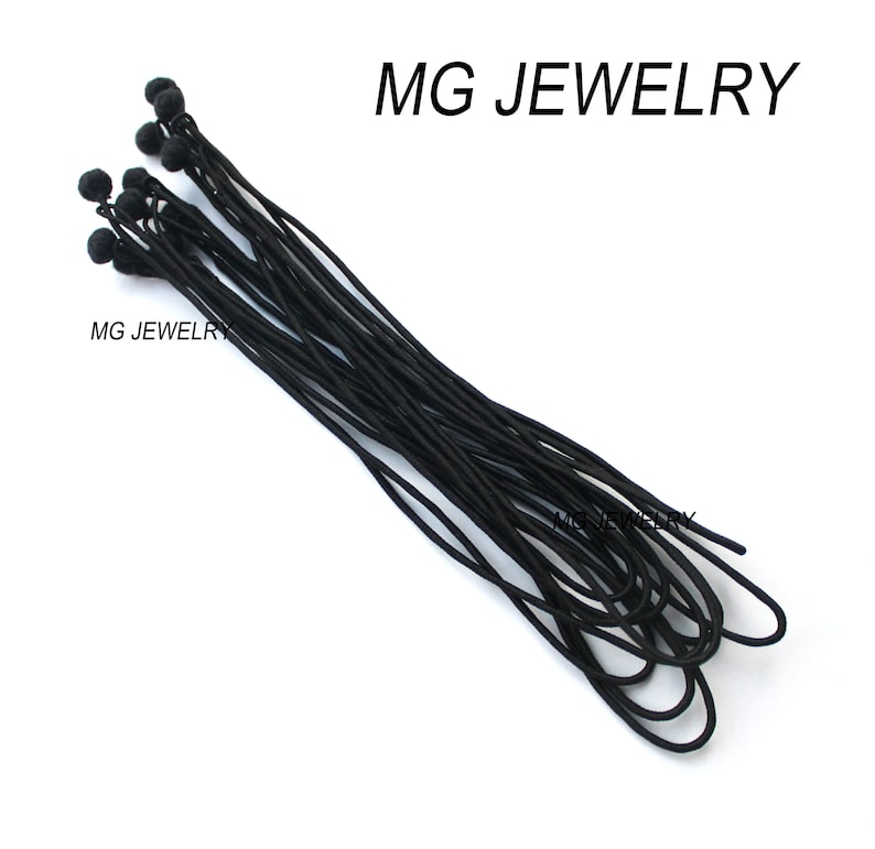 May include: A bundle of black elastic cord with small black ball ends.  MG JEWELRY is printed on the white background.
