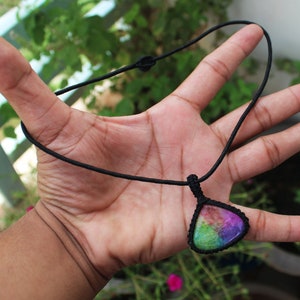 May include: A rainbow-colored gemstone pendant on a black cord necklace. The pendant is a teardrop shape and has a variety of colors, including pink, purple, green, and blue.