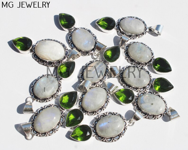 May include: A group of 10 silver pendants with oval moonstone and pear-shaped green peridot gemstones. The pendants have a decorative filigree design around the stones.
