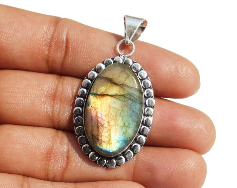 May include: Silver pendant featuring a large oval-shaped labradorite gemstone with iridescent green, gold, and blue hues. The stone is set in a silver bezel with a beaded border.