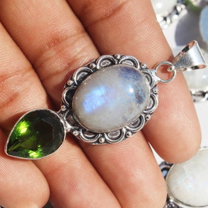May include: A silver pendant with a large oval moonstone and a smaller pear-shaped green gemstone. The pendant has an ornate silver frame.