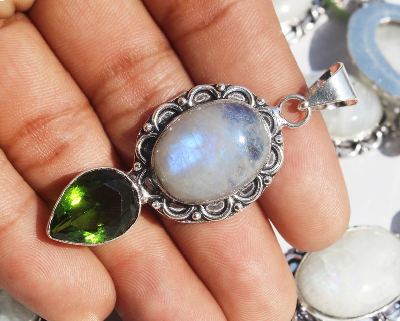 May include: A silver pendant with a large oval moonstone and a smaller pear-shaped green gemstone. The pendant has an ornate silver frame.
