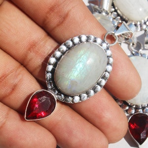 May include: A silver pendant with a large oval moonstone and a smaller teardrop-shaped red gemstone. The moonstone has a rainbow sheen.