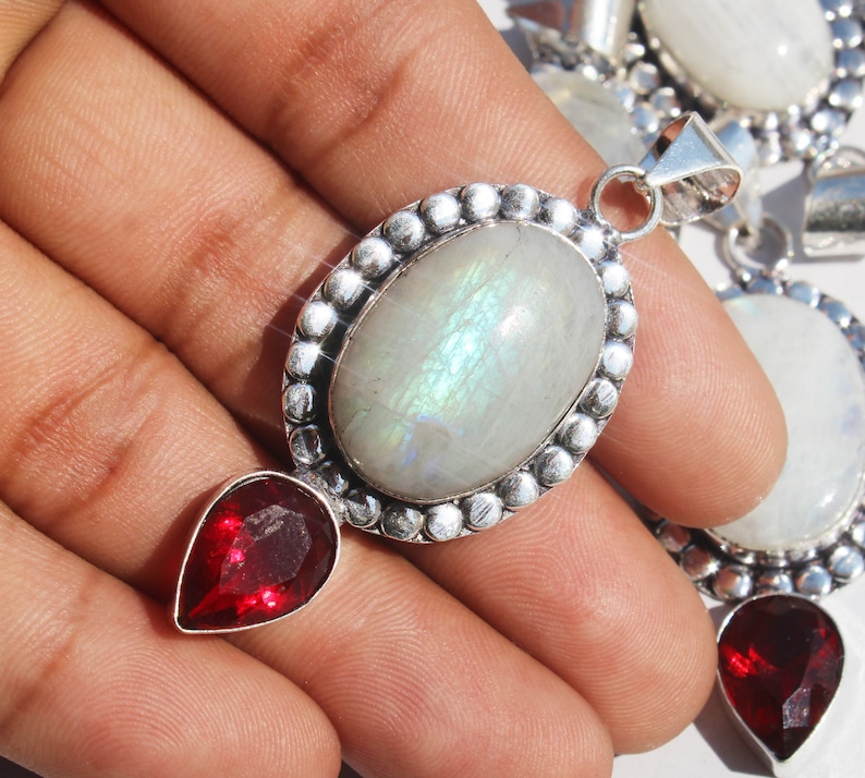 May include: A silver pendant with a large oval moonstone and a smaller teardrop-shaped red gemstone. The moonstone has a rainbow sheen.