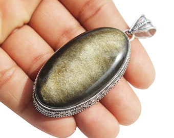 May include: A silver pendant with a large oval-shaped golden obsidian gemstone. The pendant has a detailed silver border and a silver bail.