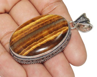May include: A silver pendant with an oval-shaped tiger's eye gemstone. The pendant has an intricate silver design around the edge.