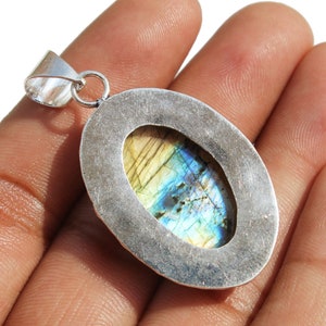 May include: Silver pendant with a large oval-shaped labradorite gemstone. The gemstone has a blue, green, and gold iridescent sheen.