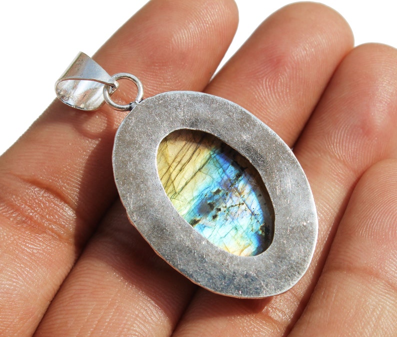 May include: Silver pendant with a large oval-shaped labradorite gemstone. The gemstone has a blue, green, and gold iridescent sheen.